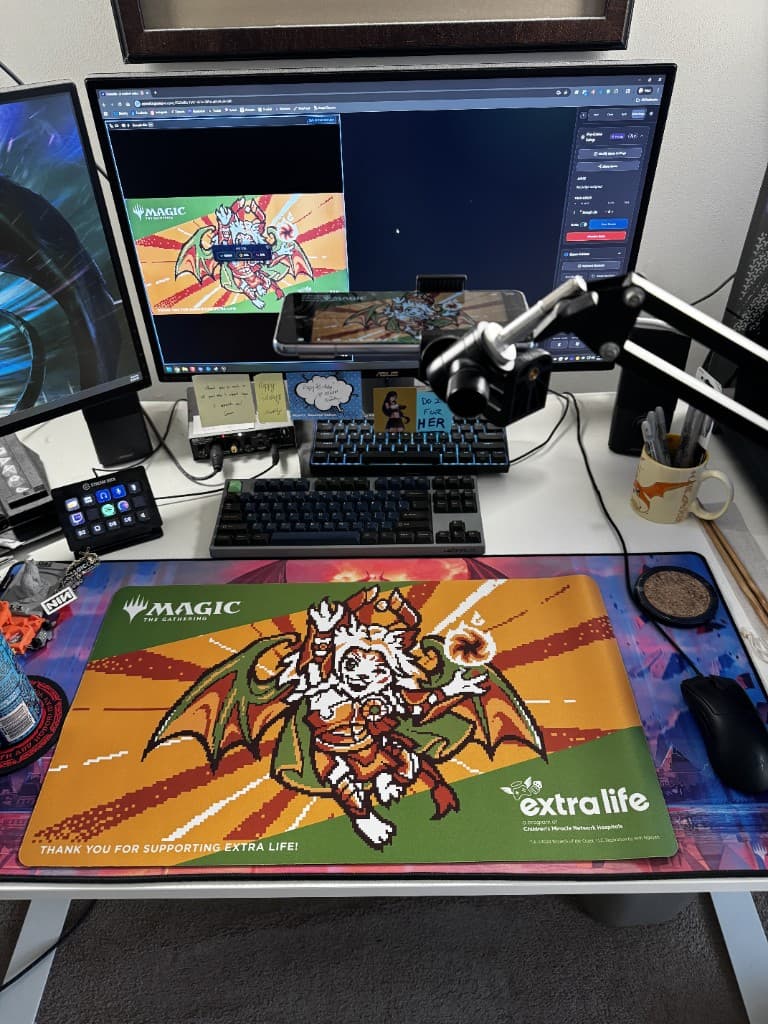 Dual-monitor desk with phone on an articulating arm aimed at an MTG playmat
